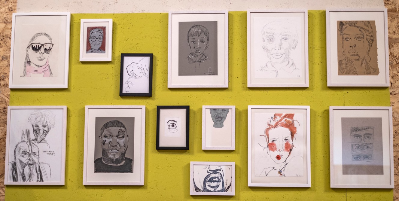 Zeichnungen von Gesichtern oder Gesichtspartien, gerahmt, an einer Wand hängend